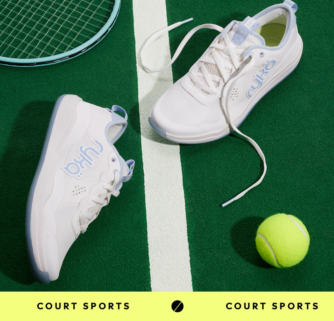 A pair of women's white tennis shoes with blue accents laying on a tennis court next to a tennis ball. A yellow banner below says 