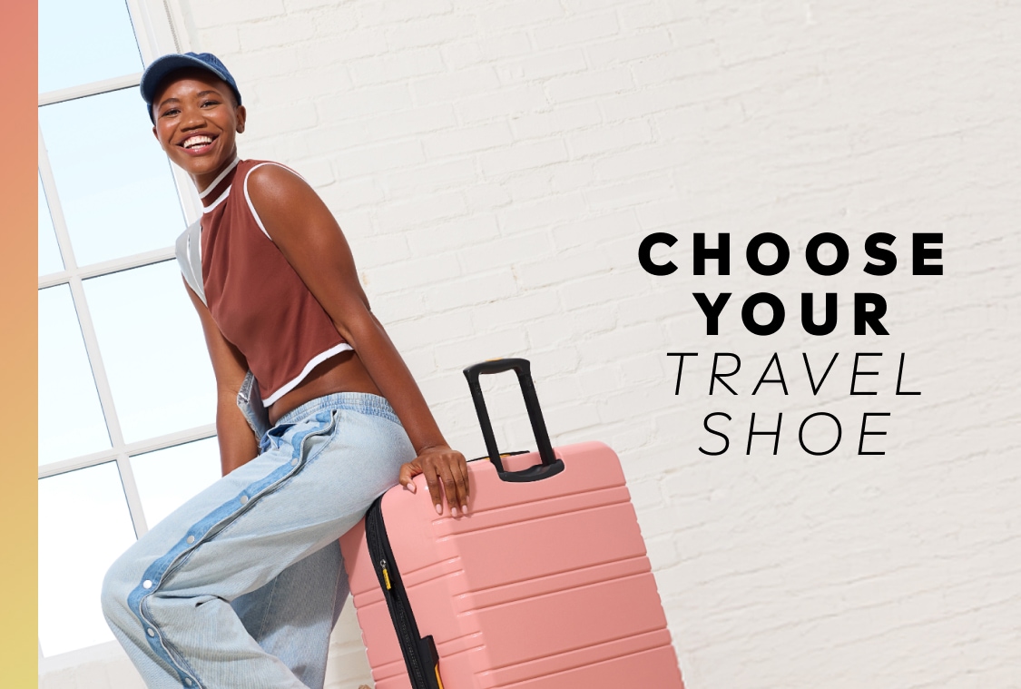 A woman wearing a brown top, jeans, and a hat, sitting on a pink suitcase with text reading 
