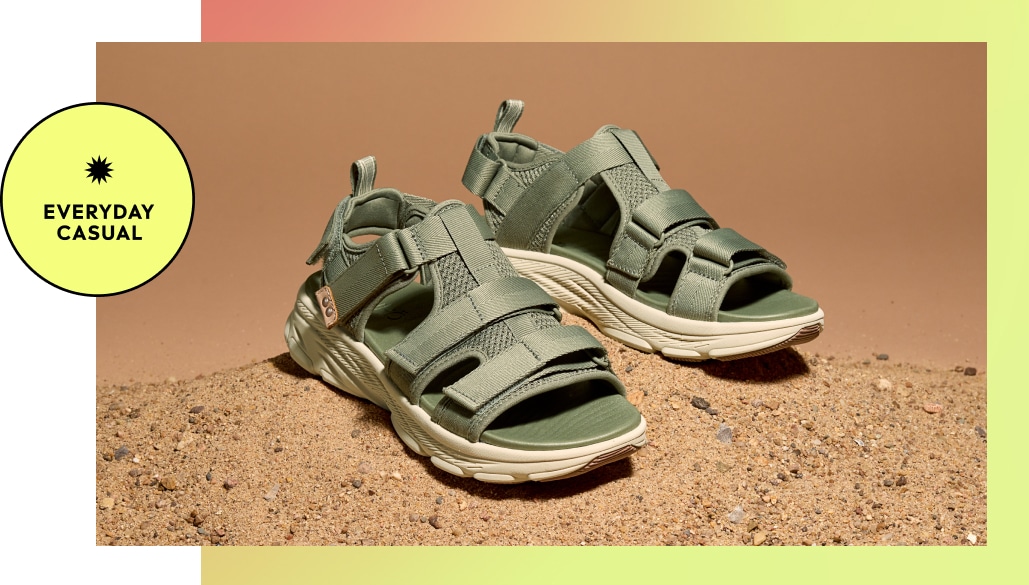 A pair of green strappy women's athletic sandals on a sandy background. A yellow graphic says 