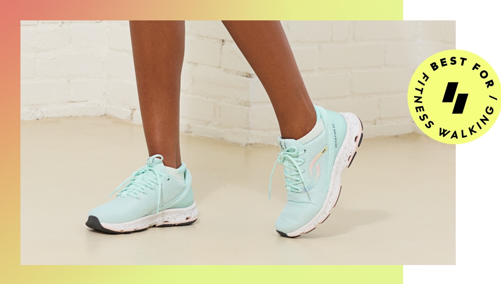 A woman wearing a pair of mint green walking sneakers with a yellow graphic saying 