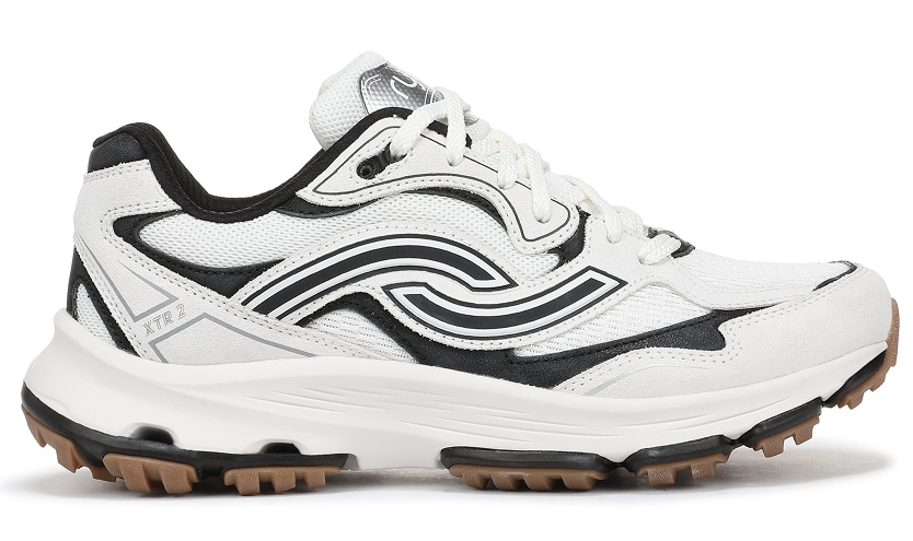 A side view of a women's white walking sneaker with black detailing, chunky sole, and textured gum outsole.