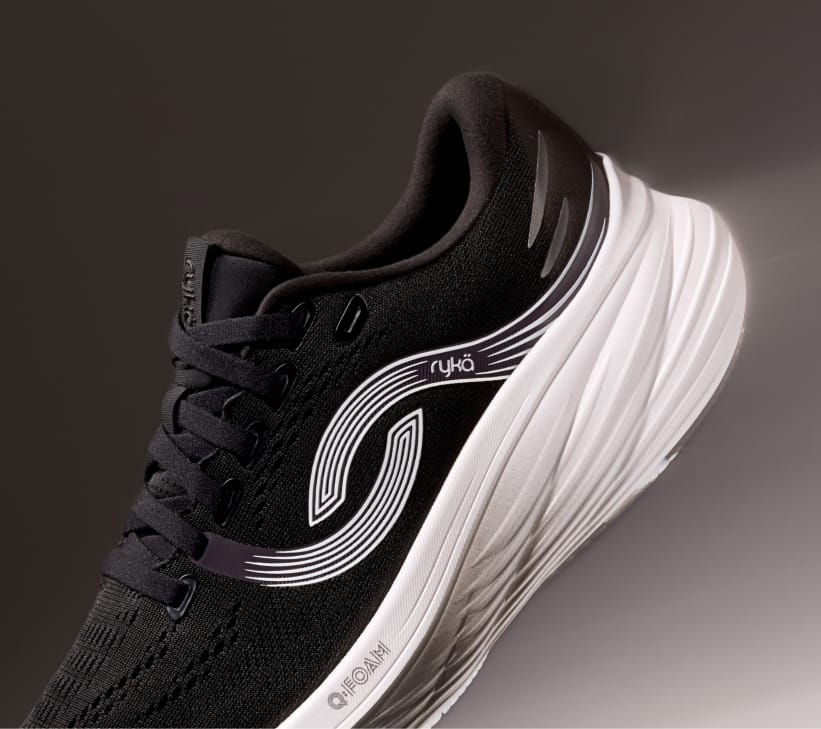 A black women's running sneaker with a white sole displayed at an angle on a black background. 