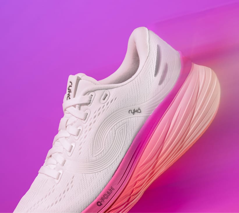 A pink women's running sneaker with an orange and purple sole displayed at an angle on a purple background. 
