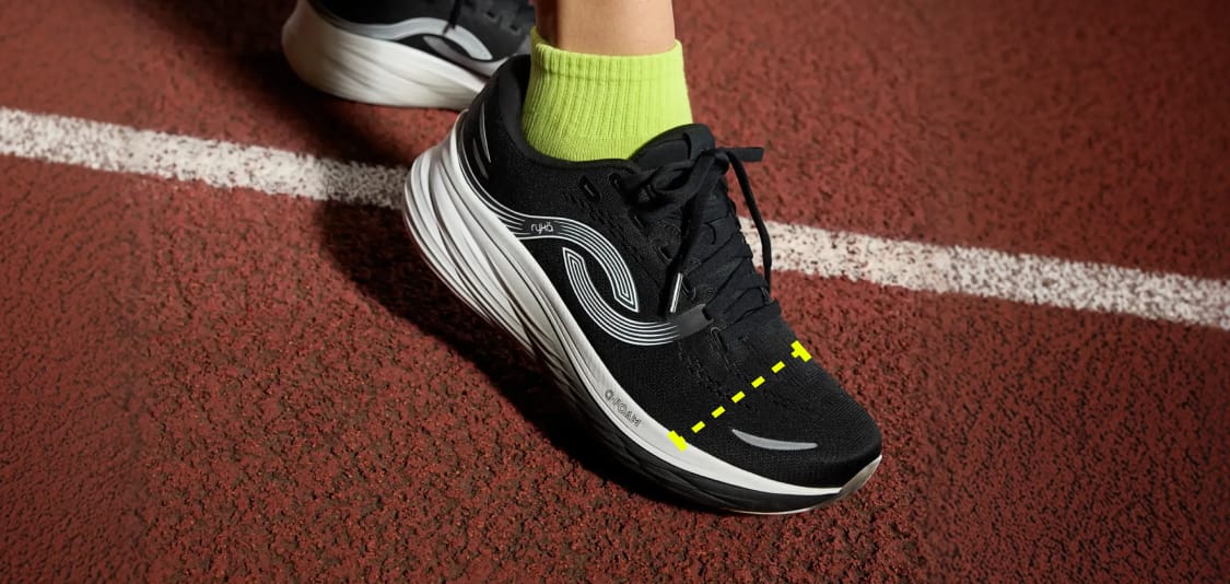 Woman on a track wearing a pair of black and white running shoes with a bright geometric graphic overlay highlighting the forefoot fit.