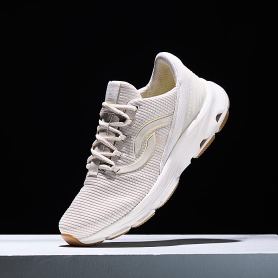 Women's beige sneaker with a white sole displayed at an angle on a black background.