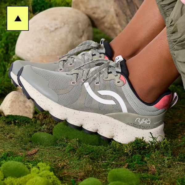 A closeup of a woman wearing gray sneakers with an off-white sole against a mossy background.