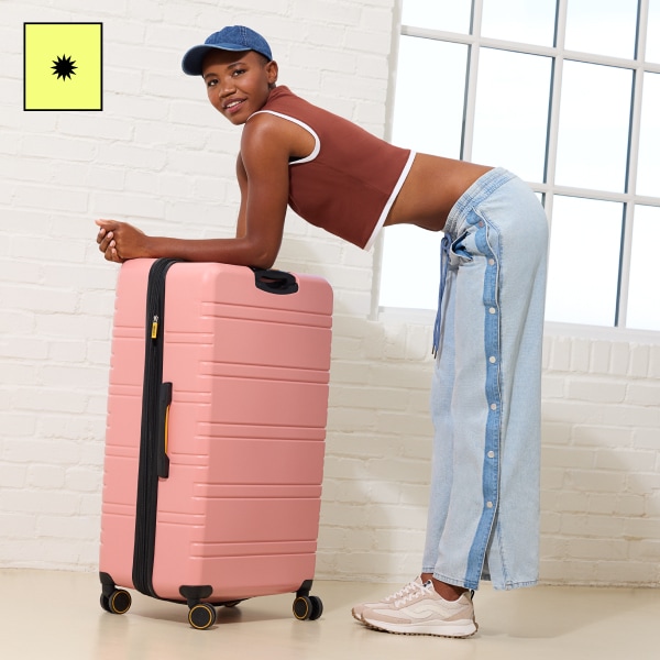 A woman leaning over a pink suitcase wearing a brown top, jeans, and a pair of pink and white retro sneakers.