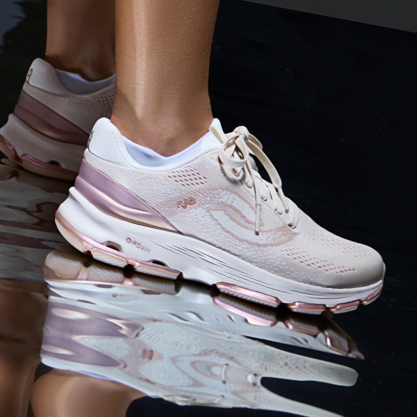 A woman wearing a pair of white sneakers with pink metallic accents near the heel and sole. 