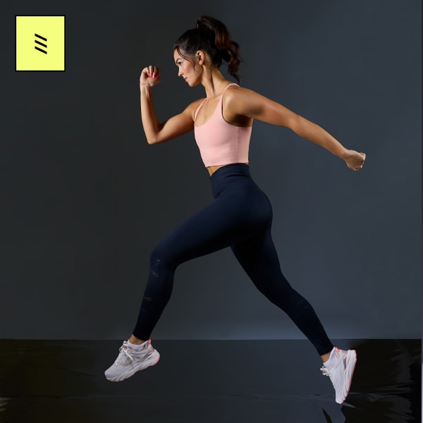 A woman running wearing a pink tank top, black leggings, and a pair of white walking sneakers with rose gold accents. 