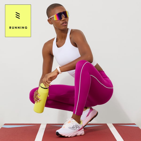 A woman wearing sunglasses, a white tank, magenta leggings, and white sneakers with a light pink sole.